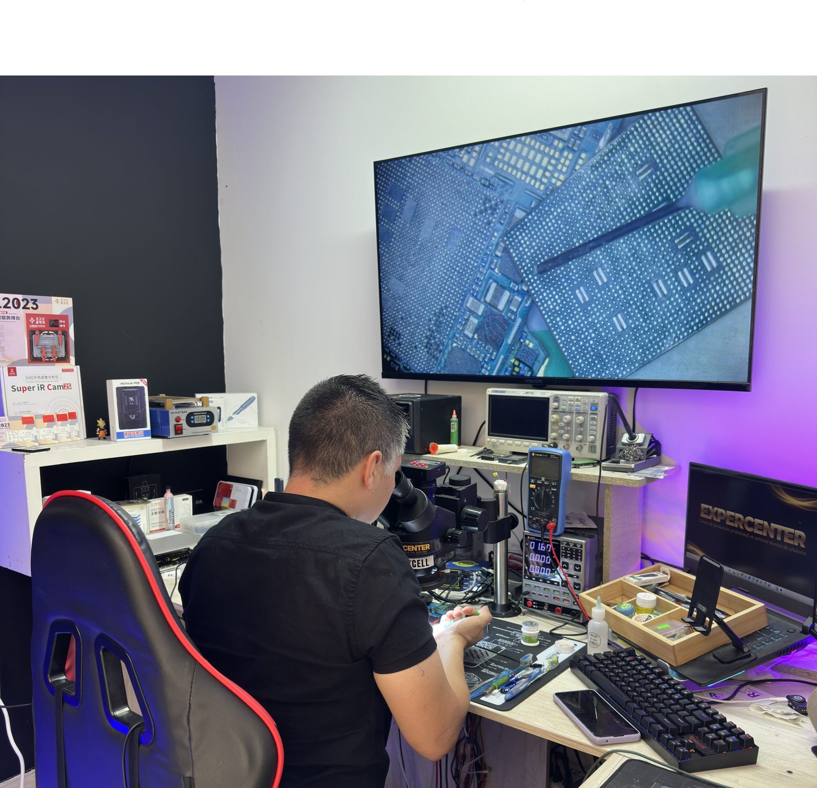 Laboratorio de microelectrónica Reparaxcell: técnico usando microscopio digital, osciloscopio y multímetro para diagnóstico de placas